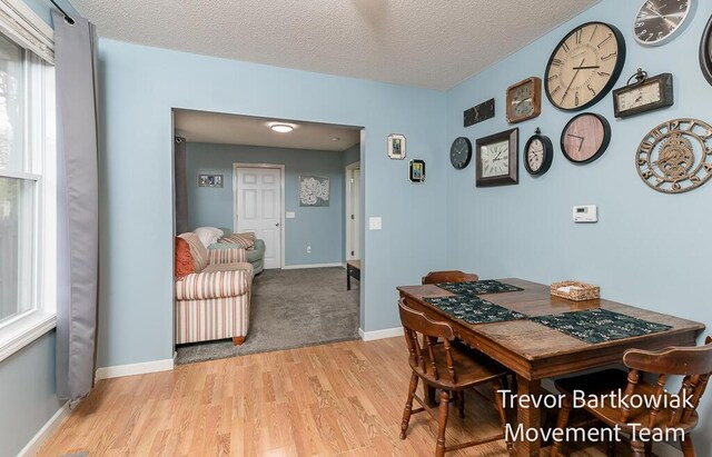 dining area with light wood-type flooring, a textured ceiling, and baseboards
