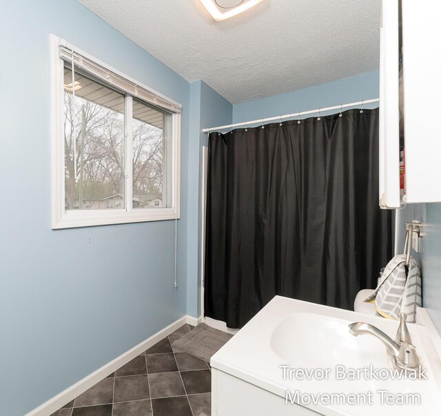 bathroom with tile patterned flooring, a sink, a textured ceiling, and baseboards