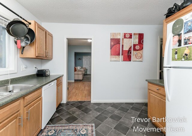 kitchen featuring dark countertops, white appliances, a textured ceiling, baseboards, and dark tile patterned floors