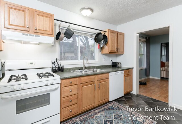 kitchen featuring dark countertops, a sink, white appliances, a textured ceiling, and under cabinet range hood