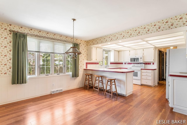 kitchen with white appliances, a peninsula, wallpapered walls, and visible vents