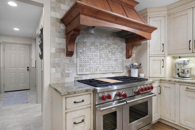 326 Greentree Ln NE, Ada, MI 49301 - kitchen with range with two ovens, premium range hood, backsplash, light stone counters, and recessed lighting