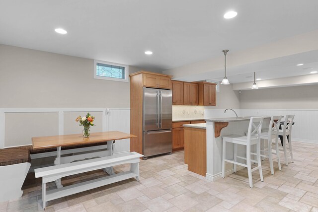 326 Greentree Ln NE, Ada, MI 49301 - kitchen featuring stainless steel refrigerator, a kitchen bar, light stone finish floors, a wainscoted wall, and decorative light fixtures
