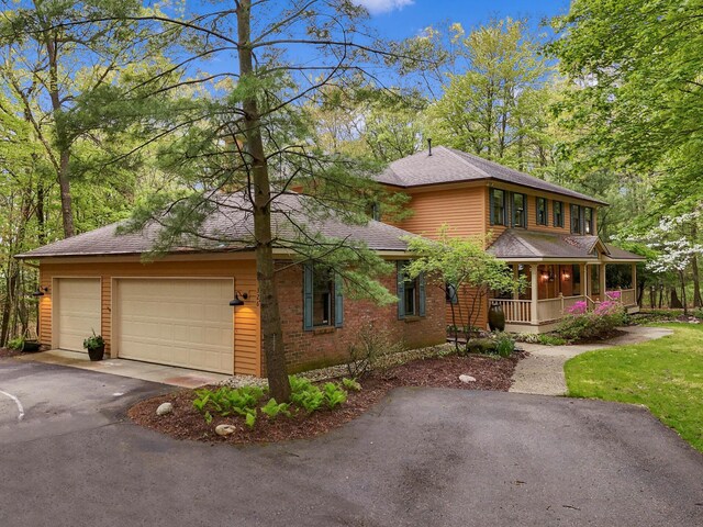 326 Greentree Ln NE, Ada, MI 49301 - view of front facade with a porch, asphalt driveway, an attached garage, roof with shingles, and brick siding