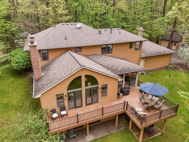 326 Greentree Ln NE, Ada, MI 49301 - rear view of property featuring a deck, a lawn, outdoor dining area, a shingled roof, and a forest view