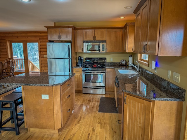 9184 S M-37 Hwy, Wellston, MI 49689 - kitchen featuring appliances with stainless steel finishes, a sink, light wood-style floors, rustic walls, and a kitchen breakfast bar