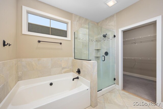full bathroom featuring baseboards, a shower stall, a walk in closet, and a bath