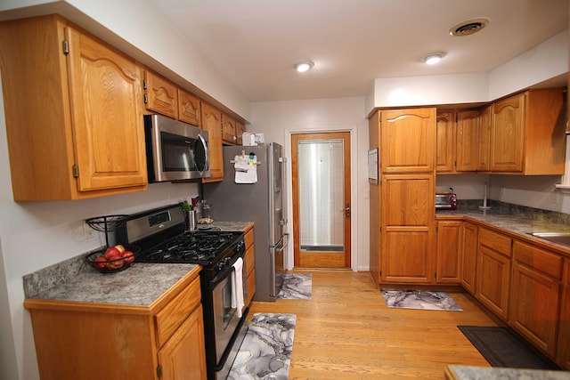 53240 Hemlock Lake Rd, Marcellus, MI 49067 - kitchen with stainless steel appliances, light wood-style flooring, brown cabinetry, a sink, and dark countertops
