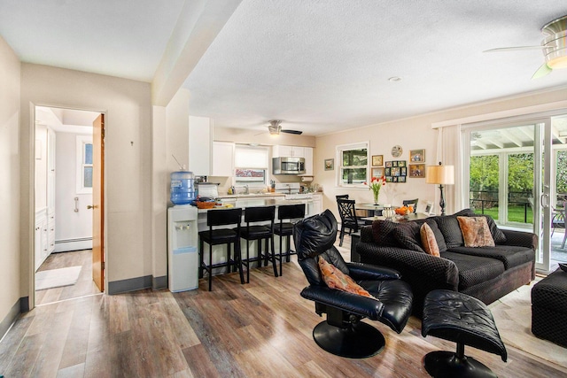 living area featuring baseboards, ceiling fan, a baseboard heating unit, and wood finished floors