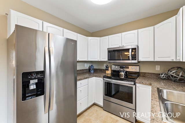 kitchen featuring dark countertops, white cabinets, a sink, light tile patterned floors, and stainless steel appliances