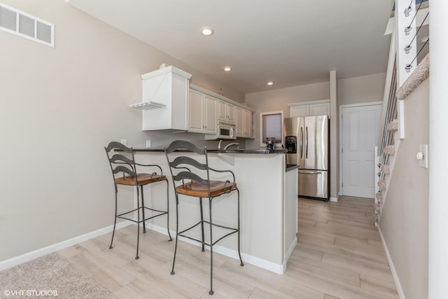 257 Shoreview Way Unit 9, Saint Joseph, MI 49085 - kitchen featuring white microwave, stainless steel fridge, a peninsula, light wood-type flooring, and a breakfast bar