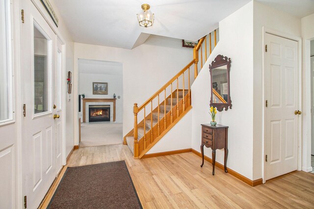 entrance foyer featuring baseboards, a fireplace, wood finished floors, and stairway