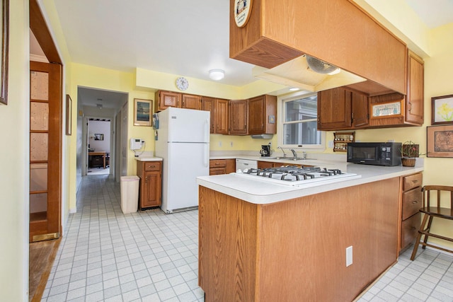 kitchen with brown cabinets, light countertops, a sink, a peninsula, and white appliances