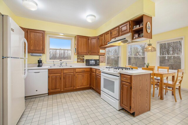 kitchen with a sink, light countertops, a peninsula, under cabinet range hood, and white appliances