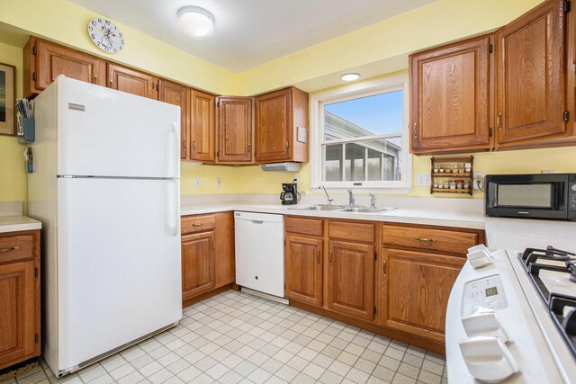 kitchen featuring a sink, white appliances, light countertops, brown cabinetry, and light tile patterned floors