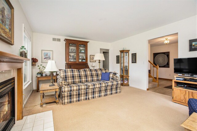 living area with visible vents, stairs, baseboards, light colored carpet, and a tile fireplace