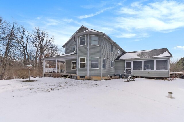 snow covered house featuring covered porch and a sunroom