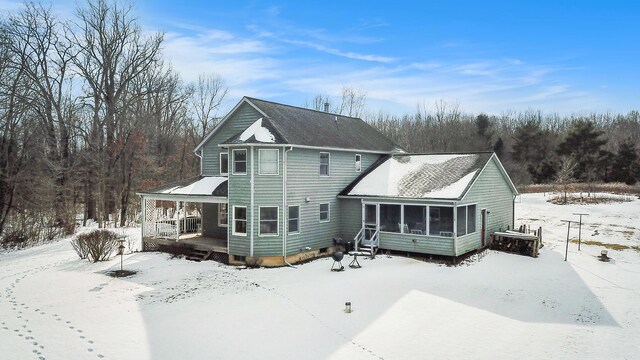 snow covered back of property with covered porch and a sunroom