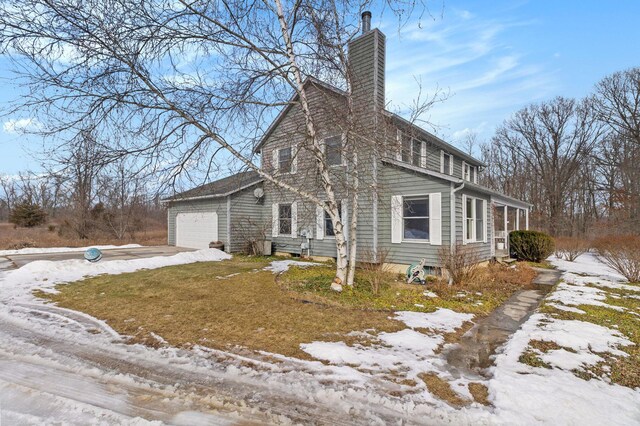 view of snow covered exterior featuring a yard, an attached garage, driveway, and a chimney