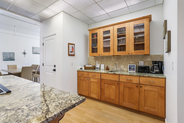 532 Dyckman Ave Unit B1A, South Haven, MI 49090 - kitchen with light wood-style floors, light stone counters, decorative backsplash, a sink, and brown cabinetry
