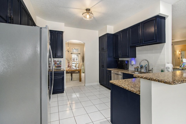 6847 Northstar Ave, Kalamazoo, MI 49009 - kitchen featuring freestanding refrigerator, a sink, arched walkways, light tile patterned floors, and dark stone countertops