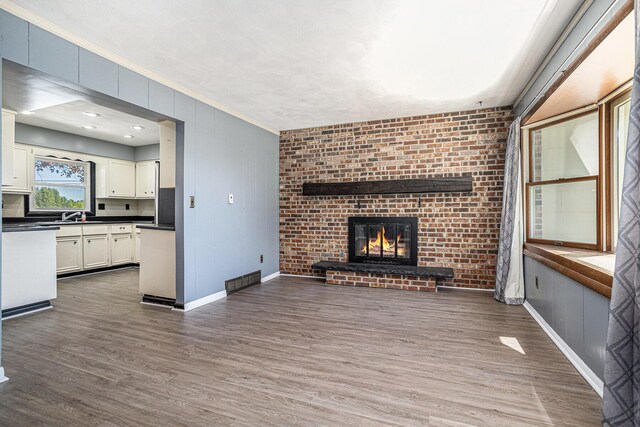 105 N Dr E, Marshall, MI 49068 - unfurnished living room featuring dark wood-type flooring, crown molding, a brick fireplace, baseboards, and a sink