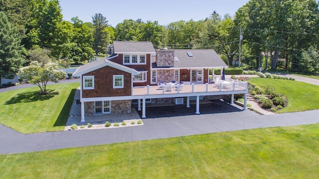 view of front of home with stone siding, a wooden deck, a front lawn, driveway, and a forest view