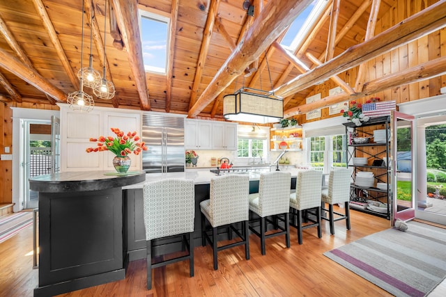 kitchen with built in refrigerator, wood ceiling, white cabinets, a skylight, and light wood finished floors