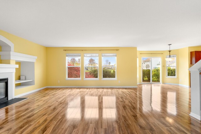unfurnished living room featuring a fireplace with flush hearth, healthy amount of natural light, and wood finished floors