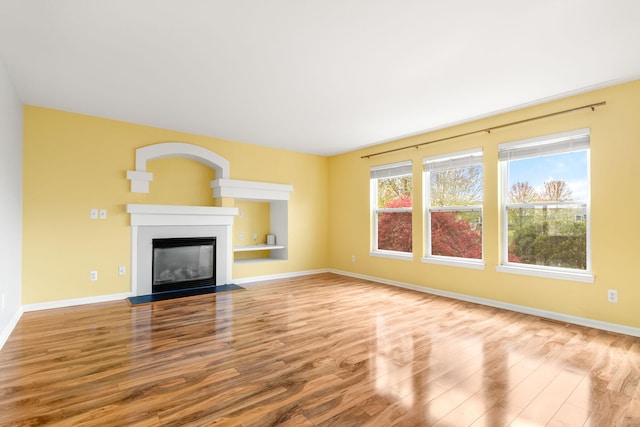 unfurnished living room featuring wood finished floors, baseboards, and a glass covered fireplace