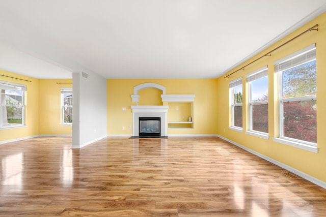 unfurnished living room featuring wood finished floors, healthy amount of natural light, baseboards, and a fireplace with flush hearth
