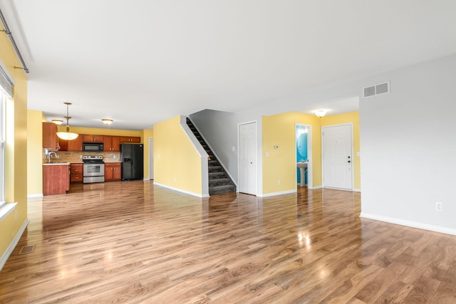 unfurnished living room with a sink, light wood-style flooring, stairs, and baseboards