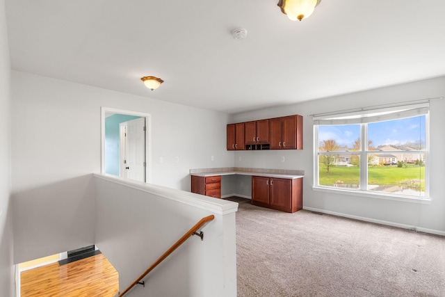 kitchen featuring light colored carpet, light countertops, baseboards, and brown cabinets