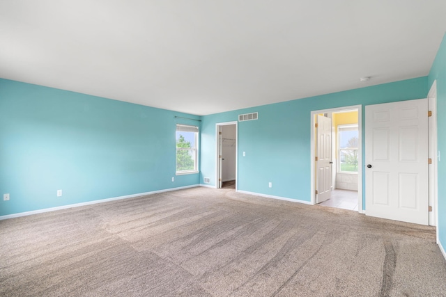 unfurnished bedroom with carpet flooring, baseboards, a walk in closet, and ensuite bath