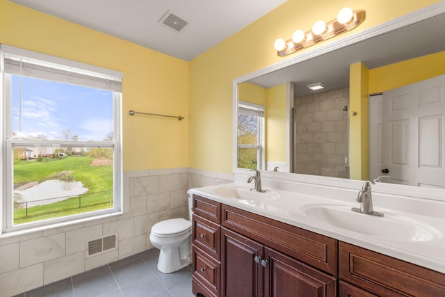 bathroom featuring tile patterned floors, toilet, tile walls, double vanity, and tiled shower