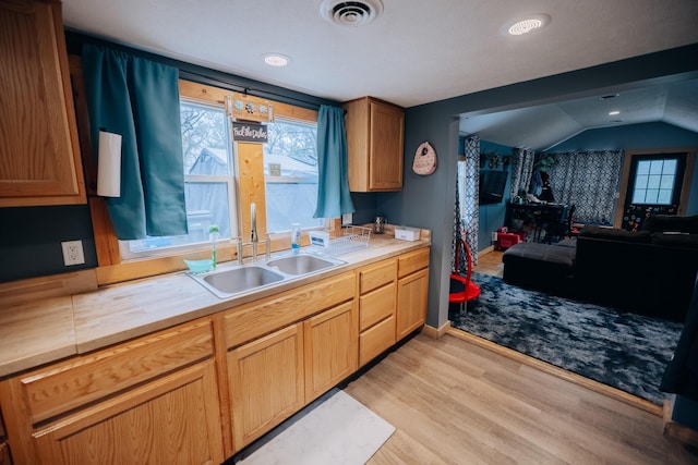 kitchen with lofted ceiling, visible vents, a sink, open floor plan, and light wood-type flooring