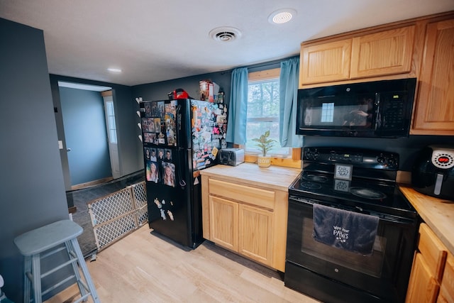 kitchen with light wood finished floors, wood counters, light brown cabinets, visible vents, and black appliances