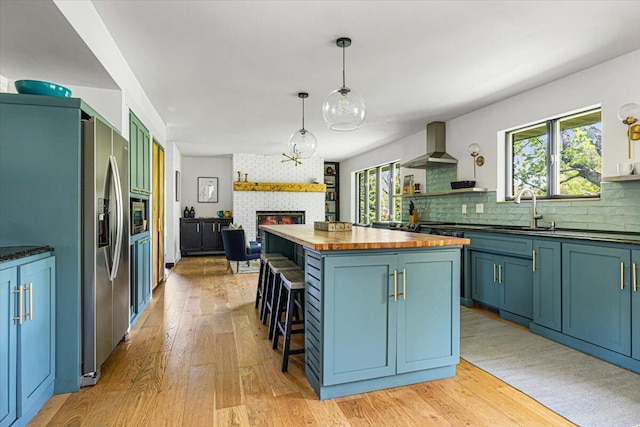 5407 Browntown Rd, Sawyer, MI 49125 - kitchen featuring butcher block countertops, a sink, wall chimney range hood, a large fireplace, and light wood-style floors