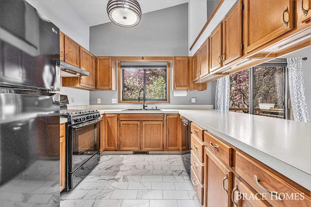 kitchen featuring black appliances, a sink, light marble finish floors, under cabinet range hood, and light countertops
