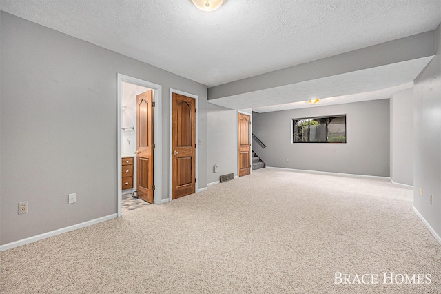 below grade area with carpet floors, a textured ceiling, stairs, and baseboards