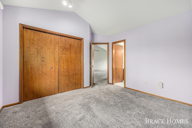 unfurnished bedroom featuring carpet, a closet, lofted ceiling, and baseboards