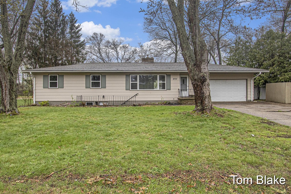 ranch-style home with an attached garage, fence, a chimney, concrete driveway, and a front lawn