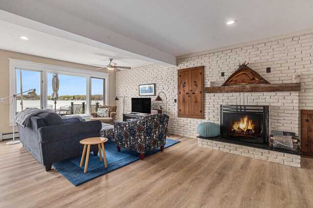 447 Paradise Ln, Horton, MI 49246 - living room featuring a fireplace, light wood-type flooring, a ceiling fan, beam ceiling, and a baseboard radiator
