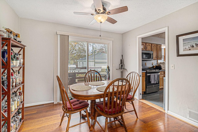 dining area featuring ceiling fan, light wood-style floors, a textured ceiling, and baseboards
