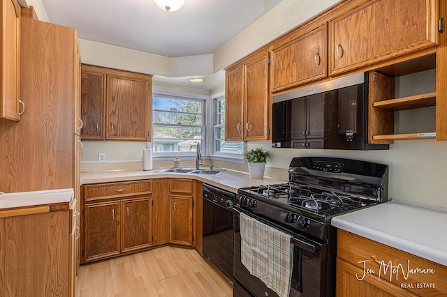 kitchen with black appliances, a sink, light wood-style flooring, and brown cabinetry