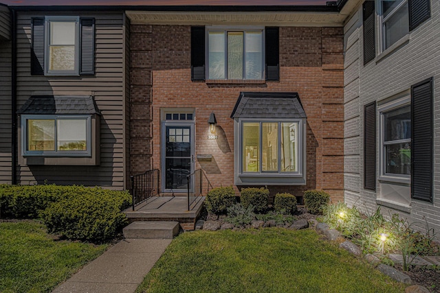 view of exterior entry with brick siding and a lawn