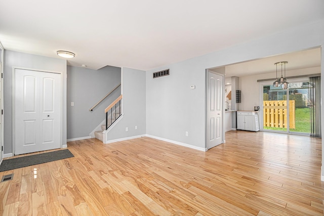 unfurnished living room featuring light wood-type flooring, visible vents, baseboards, and stairs