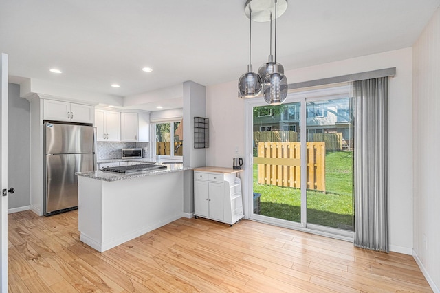 kitchen featuring a peninsula, stainless steel appliances, white cabinetry, light wood-style floors, and decorative backsplash