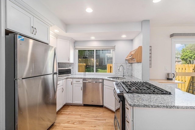 kitchen featuring a sink, a peninsula, appliances with stainless steel finishes, white cabinetry, and light wood-style floors