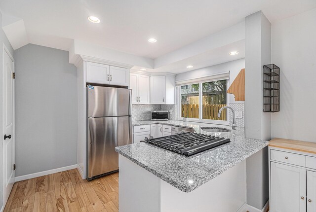 kitchen with a sink, a peninsula, stainless steel appliances, light stone counters, and white cabinetry